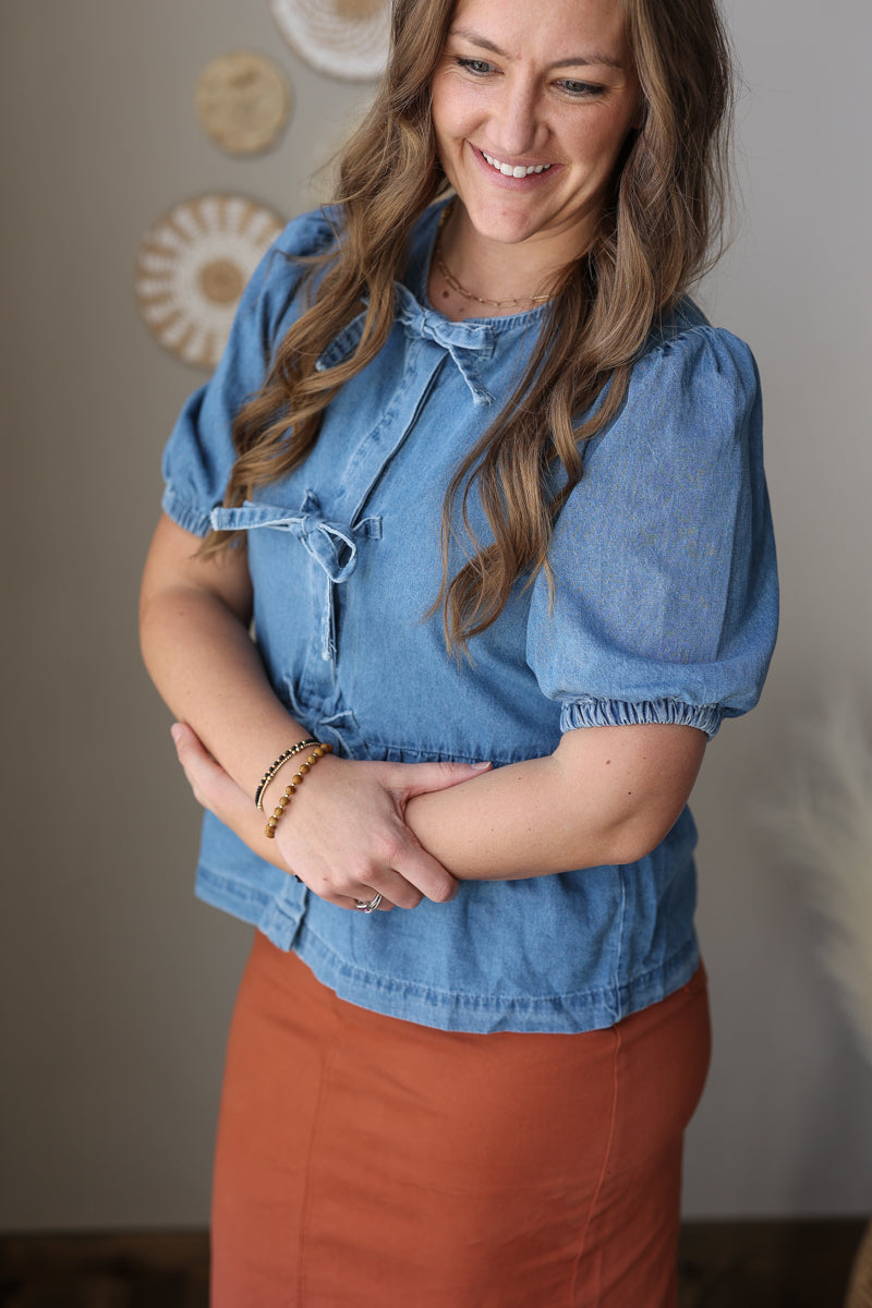 Woman wearing a blue denim blouse and orange skirt with a neutral background