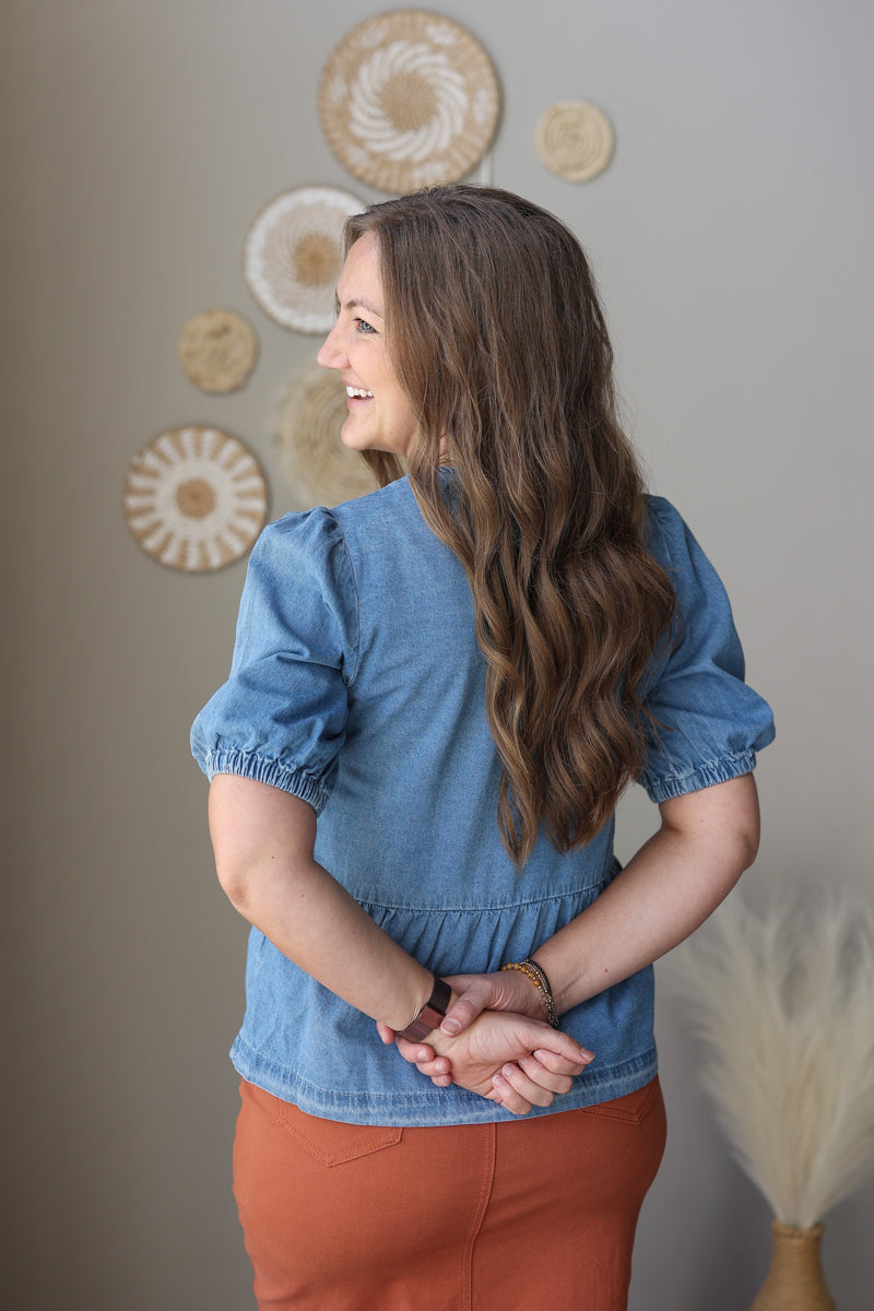 Woman wearing a blue denim top and orange midi skirt standing against a neutral wall with decorative elements.