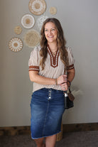 Woman wearing a striped shirt and denim skirt standing in front of decorative wall art.