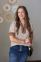 Woman wearing a striped shirt and blue jean skirt with a wall of decorative plates in the background