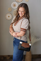 Woman holding a black and brown handbag in a room with decorative plates on the wall.