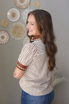 Woman wearing a striped shirt with brown accents in a room with decorative wall art.