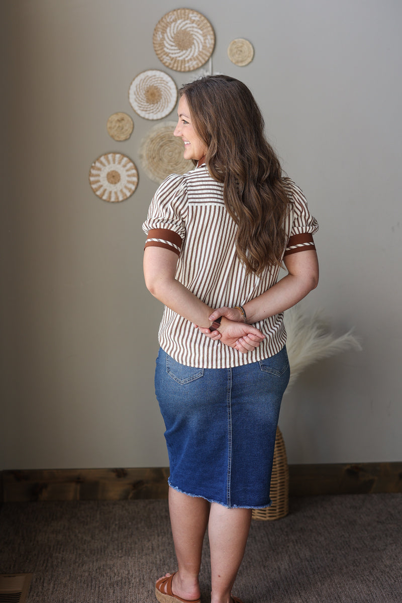 Woman wearing a striped shirt and denim skirt standing in a room with decorative wall art.