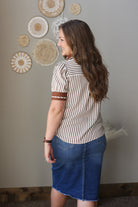 Woman wearing a striped shirt and blue skirt standing in front of decorative wall art.