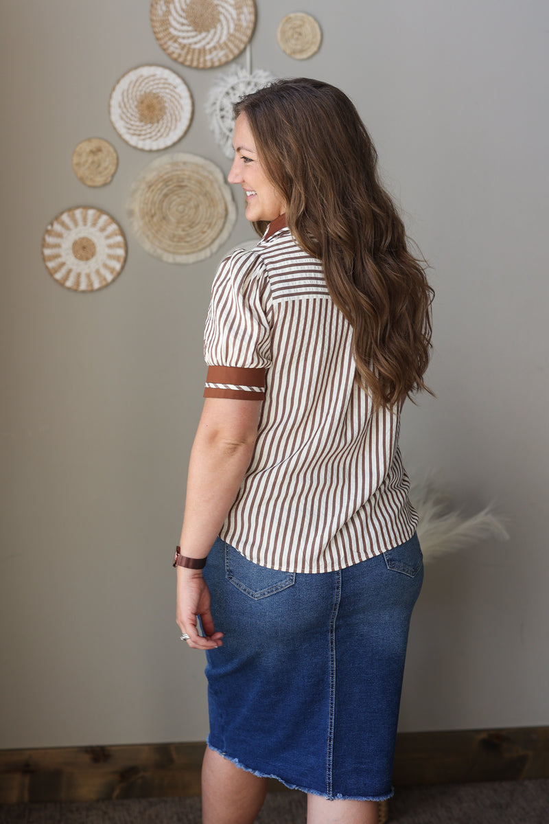 Woman wearing a striped shirt and blue skirt standing in front of decorative wall art.