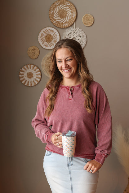 Woman in a pink long-sleeve shirt holding a coffee cup against a wall with decorative plates.