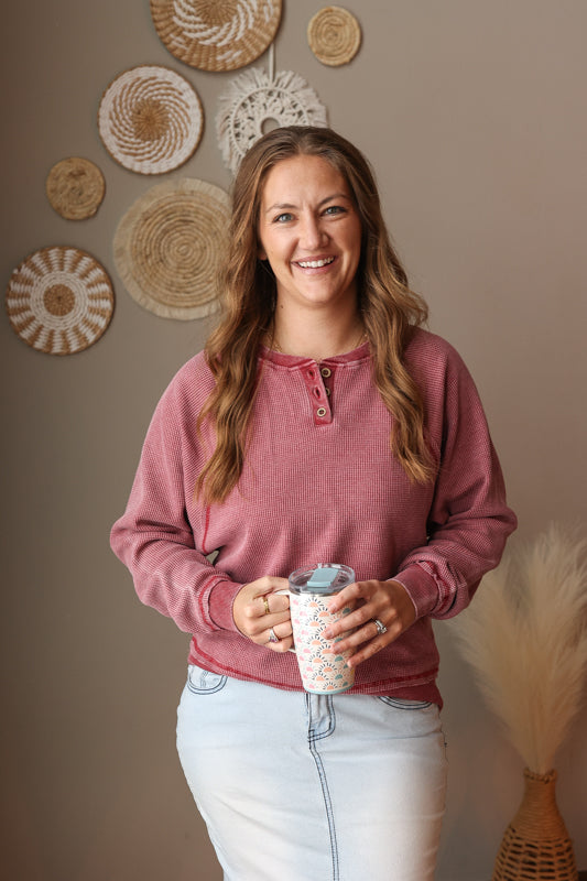 Woman in a red waffle henley shirt holding a mug with decorative wall art in the background