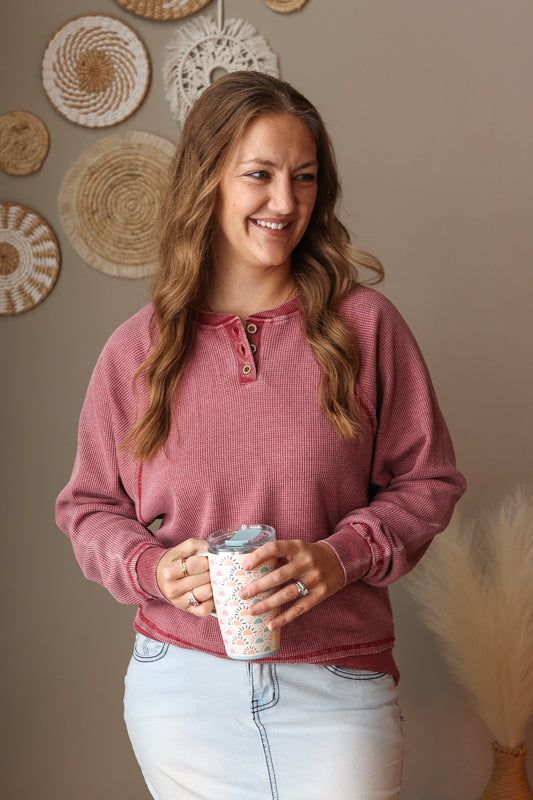 Woman in pink long-sleeve shirt holding a patterned cup against a wall with decorative plates.