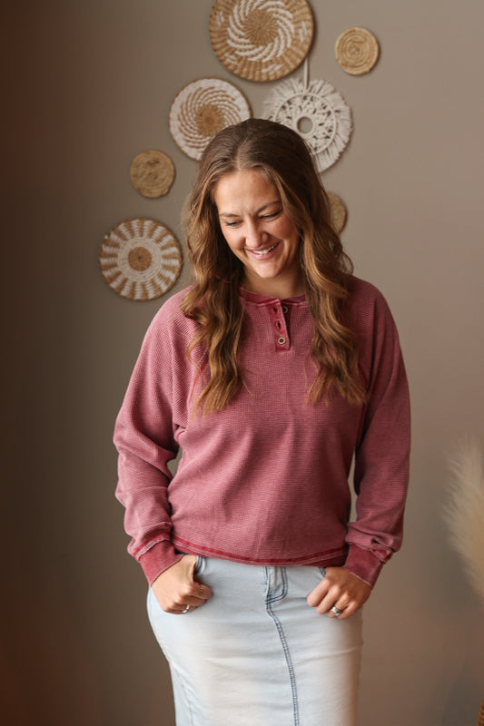 Woman wearing a pink long-sleeve shirt standing against a wall with decorative plates.