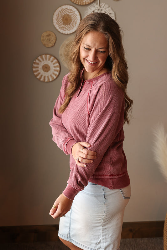 Woman wearing a burnt red sweatshirt and light blue denim skirt indoors.