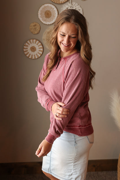 Woman wearing a burnt red sweatshirt and light blue denim skirt indoors.