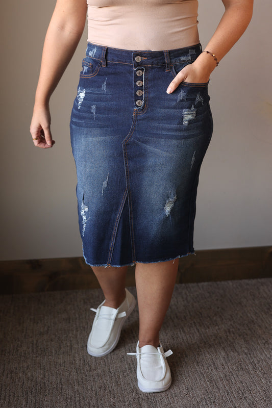 Person wearing a blue denim skirt with button details on a neutral background