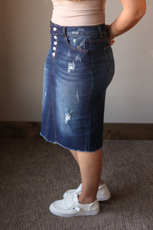 Person wearing a blue denim skirt with button details on a plain background