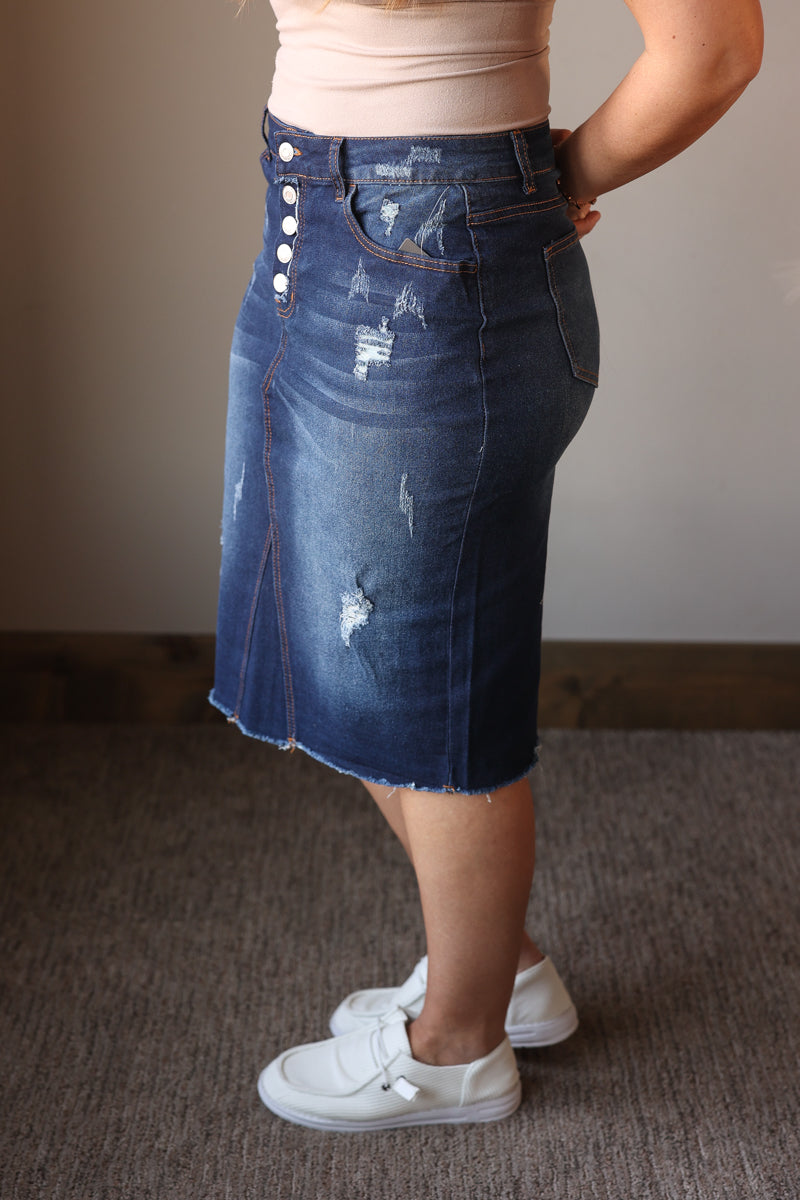 Person wearing a blue denim skirt with button details on a plain background
