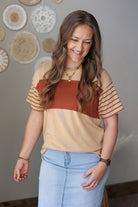 Woman wearing a beige and rust top with blue jean skirt in a room with decorative wall hangings.