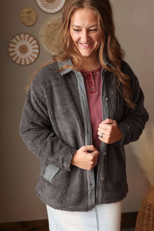 Woman wearing a gray fleece jacket indoors with decorative wall items in the background