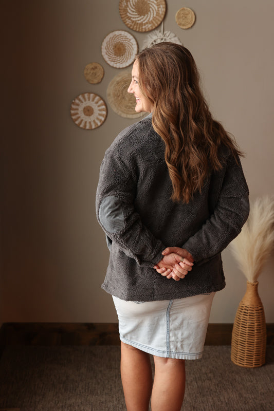 Woman wearing a dark gray sweater and light-colored denim skirt standing in a room with decorative wall art.