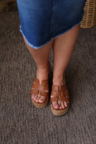 Brown woven sandals worn with a blue skirt on a textured surface