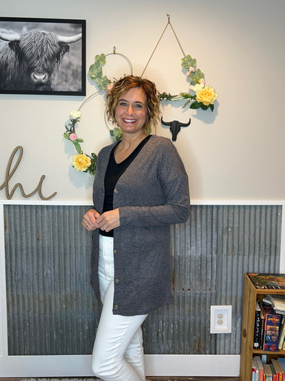 Woman wearing a spring outfit with grey cardigan, black vneck top, and white denim