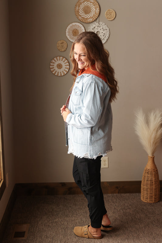 Woman wearing a sky blue denim shirt jacket layered over a cozy everyday outfit with black cargo joggers
