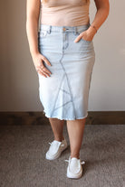 Person wearing a light blue denim skirt with a plain background