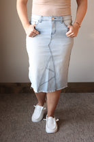 Person wearing a light blue denim skirt with a plain background