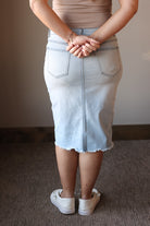 Person wearing a light blue denim skirt with a neutral background