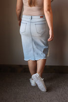 Person wearing a light blue denim skirt and white sneakers in a room with a neutral background.