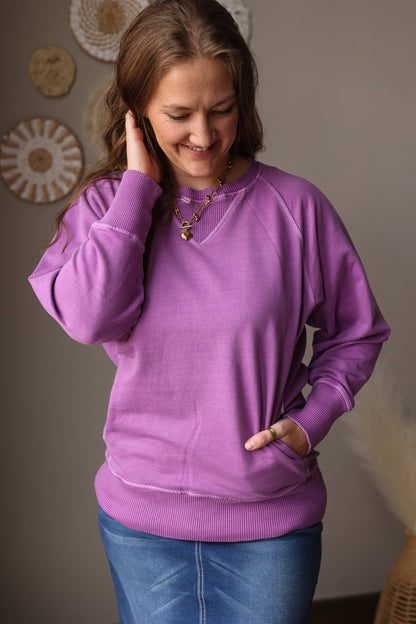 Woman wearing a purple sweater and blue jean skirt indoors with decorative plates on the wall.