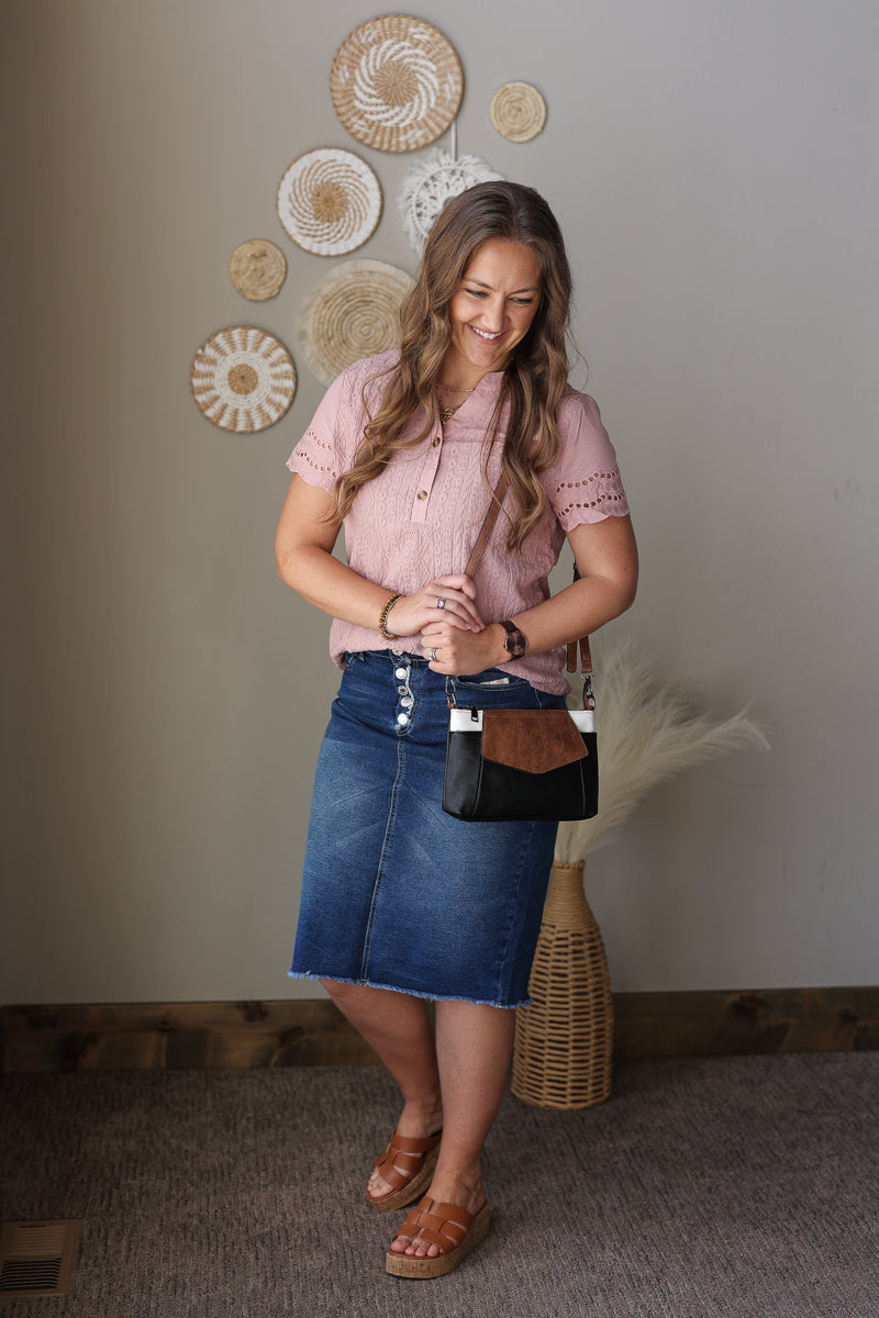 Woman in a pink shirt and blue skirt standing in a room with decorative wall art.