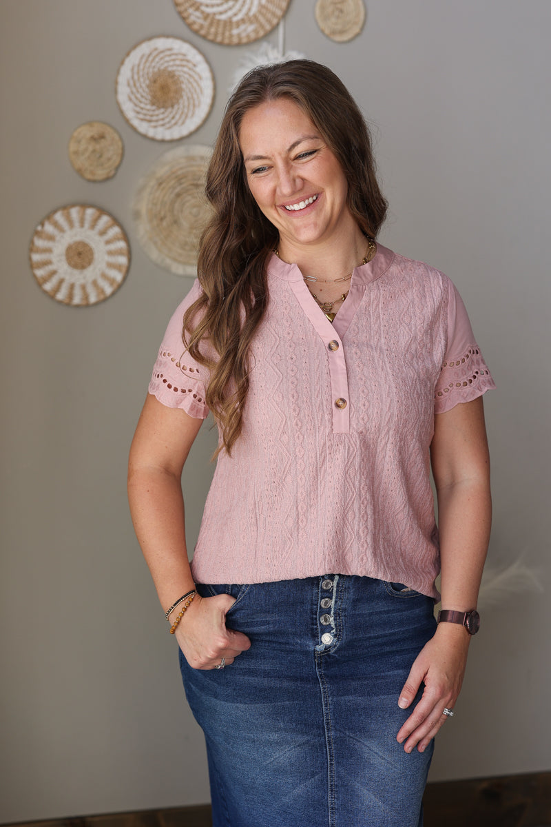 Woman wearing a pink blouse and blue jean skirt standing against a wall with decorative plates.