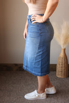 Medium Wash Fray Waist Midi Denim Skirt; stretchy denim standing against a neutral wall