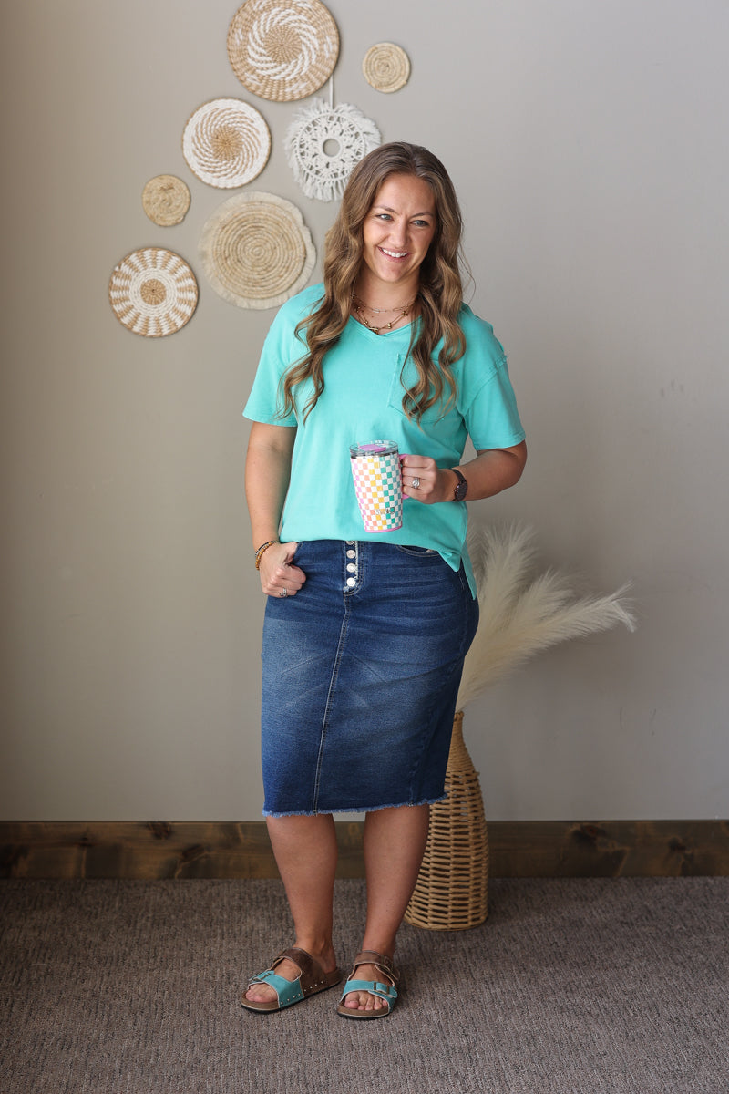 Woman in a teal shirt and denim skirt holding a polka dot cup against a wall with decorative plates.
