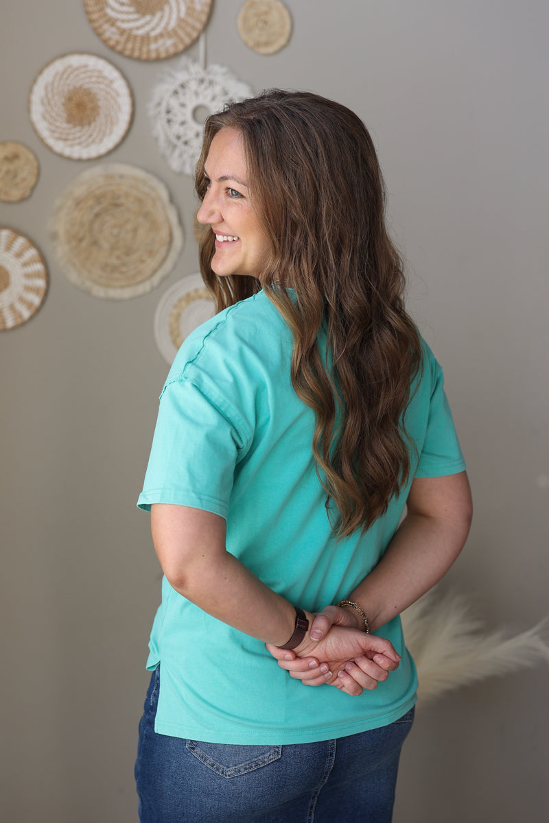 Woman wearing a turquoise shirt standing against a neutral wall with decorative plates.