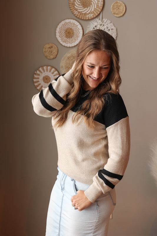 Woman wearing a beige and black sweater with decorative wall art in the background