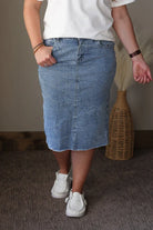 Person wearing a white t-shirt with a blue pocket design and a blue denim skirt, standing indoors.