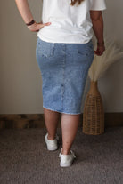 Person wearing a white t-shirt and blue denim skirt standing against a neutral background.