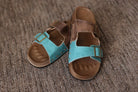 Pair of brown sandals with turquoise straps on a textured surface