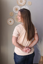 Woman wearing a beige t-shirt and blue jean denim skirt standing against a wall with decorative plates.