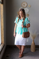 Woman in a turquoise top and white skirt standing in a room with decorative wall art.