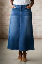 Person wearing a long blue denim skirt with a neutral background