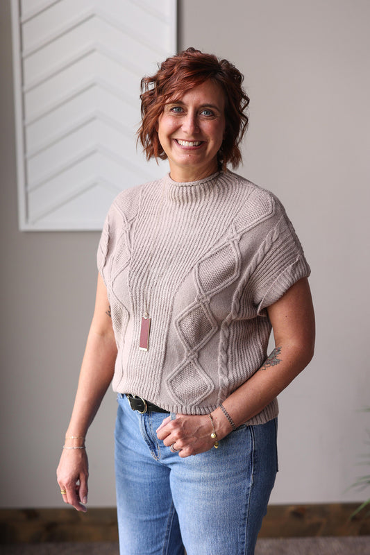 Woman wearing a beige knitted sweater and blue jeans indoors for fall fits and modest outfits