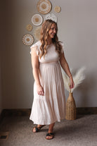 Woman in a white dress holding a decorative item in a room with wall art.