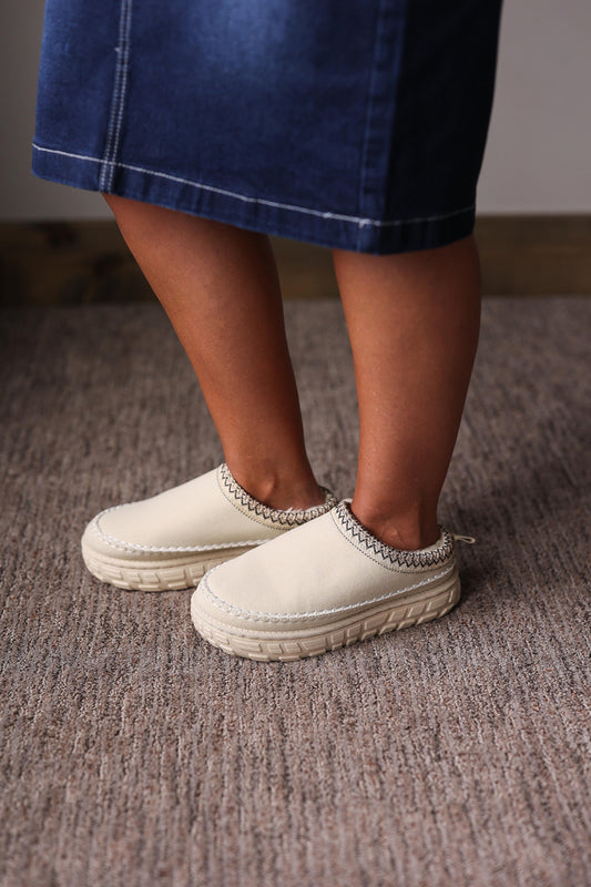 White slip-on shoes with textured sole worn by a person on a carpeted floor for casual fall outfits