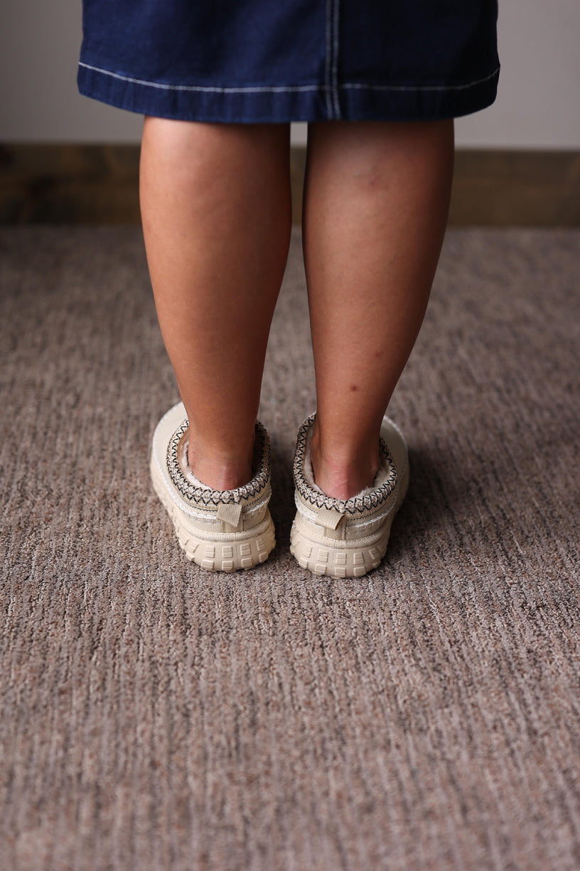 Person wearing white sandals on a carpeted floor for fall/winter outfits