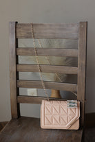 A light taupe mocha quilted leather shoulder bag with a gold chain strap, resting on a rustic wooden chair.