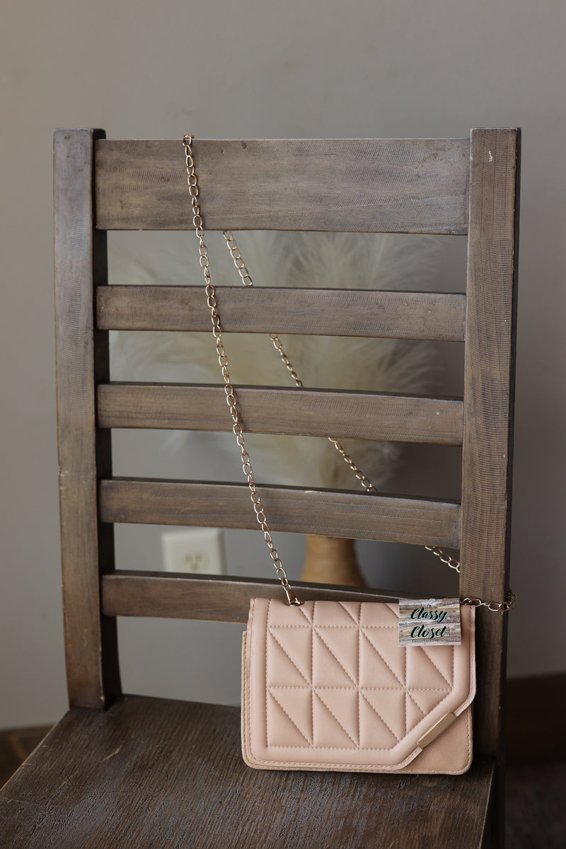 A light taupe mocha quilted leather shoulder bag with a gold chain strap, resting on a rustic wooden chair.