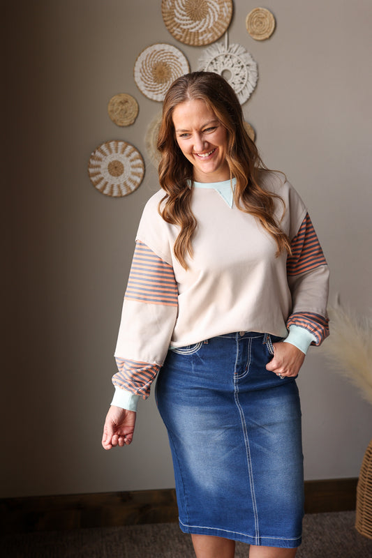woman wearing a neutral tan sweatshirt with orange and mint colorblock detail with midi denim skirt for spring outfits