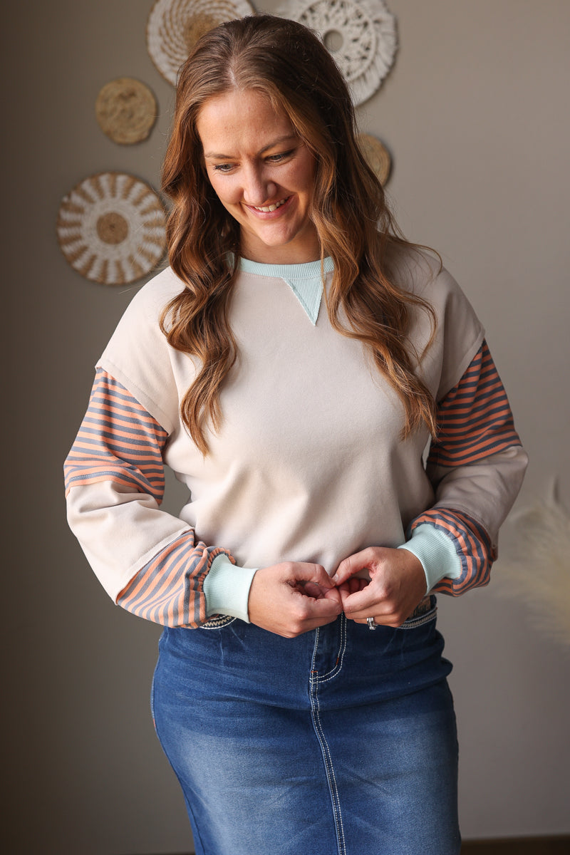 woman wearing a neutral tan sweatshirt with orange and mint colorblock detail with midi denim skirt for spring outfits or fall outfits