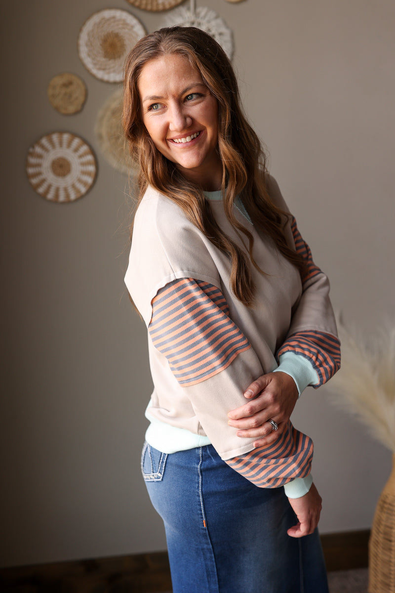 Woman wearing a striped sweater and blue jean skirt, standing against a neutral wall with decorative elements.